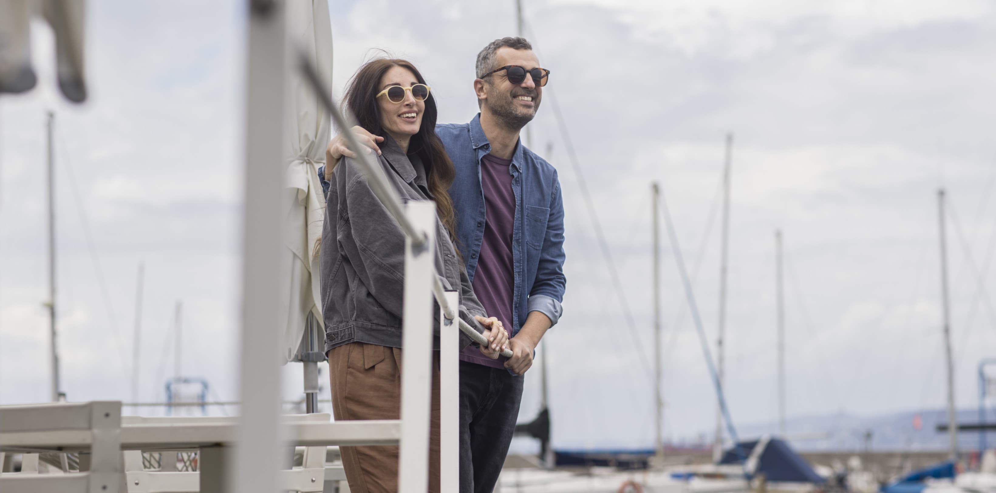 A couple is enjoying the view of the harbour in Trieste and there are several sailboats in the back.