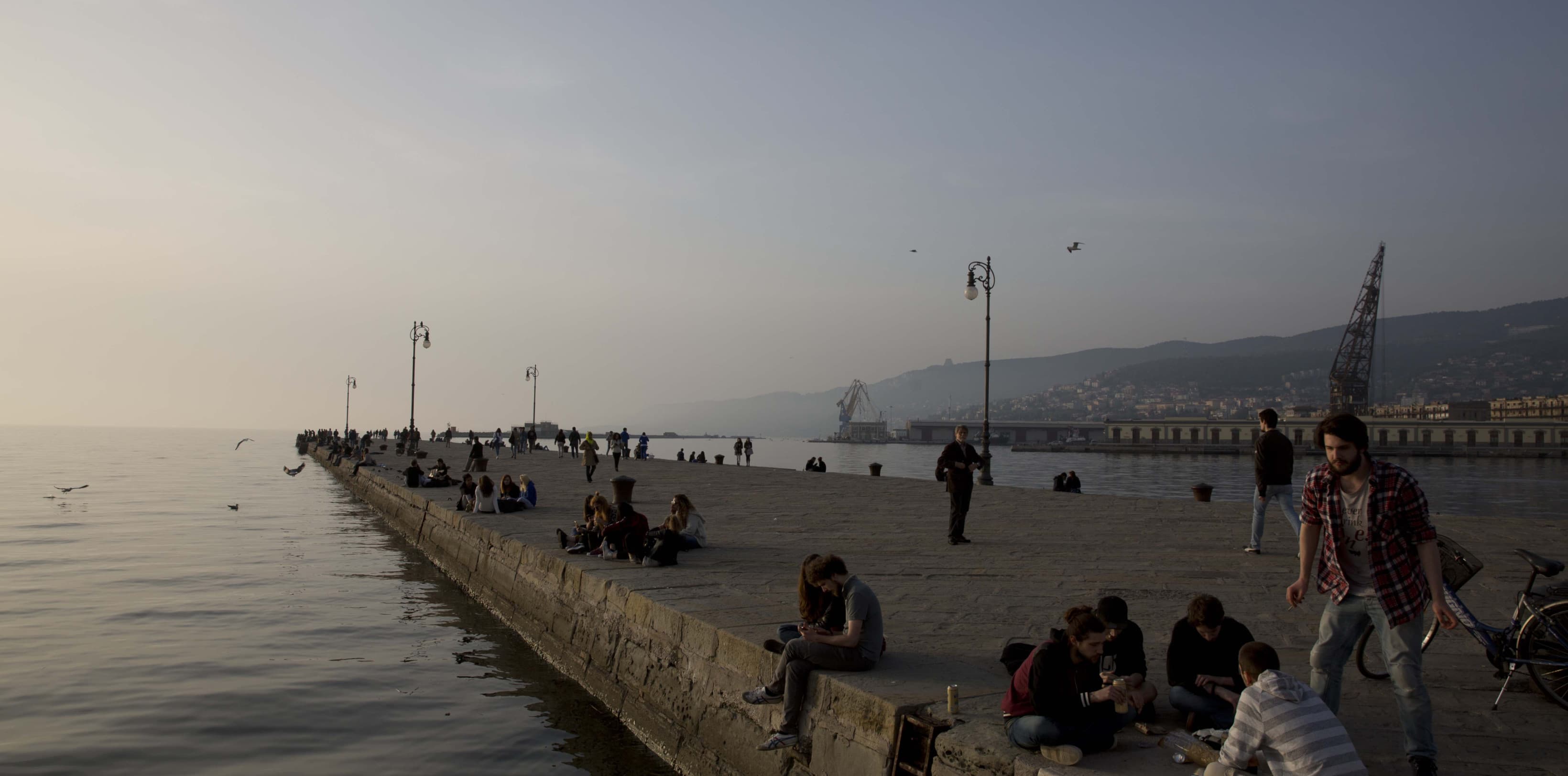 The Trieste harbour during the early morning hours. People are sitting on the harbour and enjoying the slow morning sunrise.