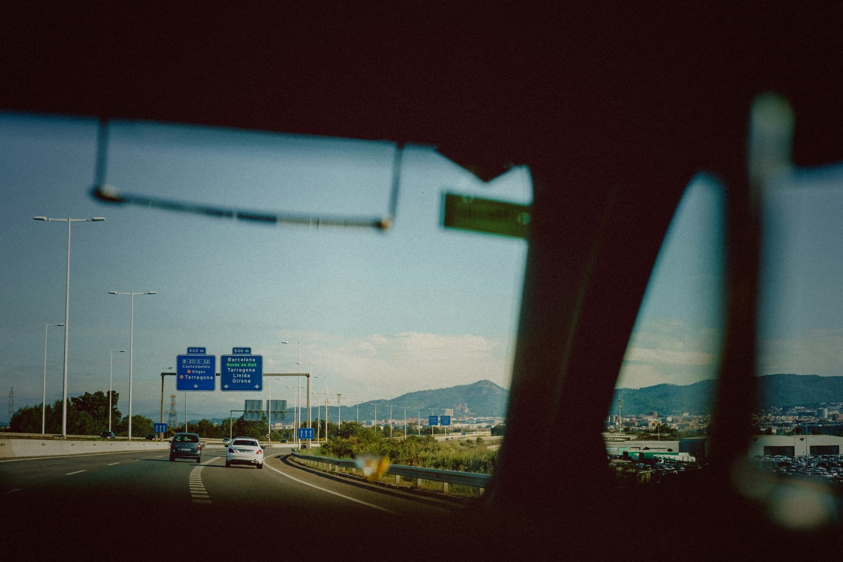 Pictured is the view point driving in a car and looking out the front window onto the highway in a southern European country like Italy. In the back you can see the mountains approaching.