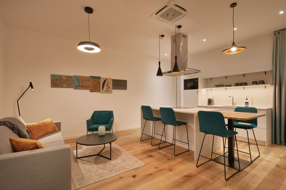 Zu sehen ist das Wohnzimmer eines Studios mit einer offenen, voll ausgestatteten Küche, das sich perfekt für einen längeren Aufenthalt eignet.