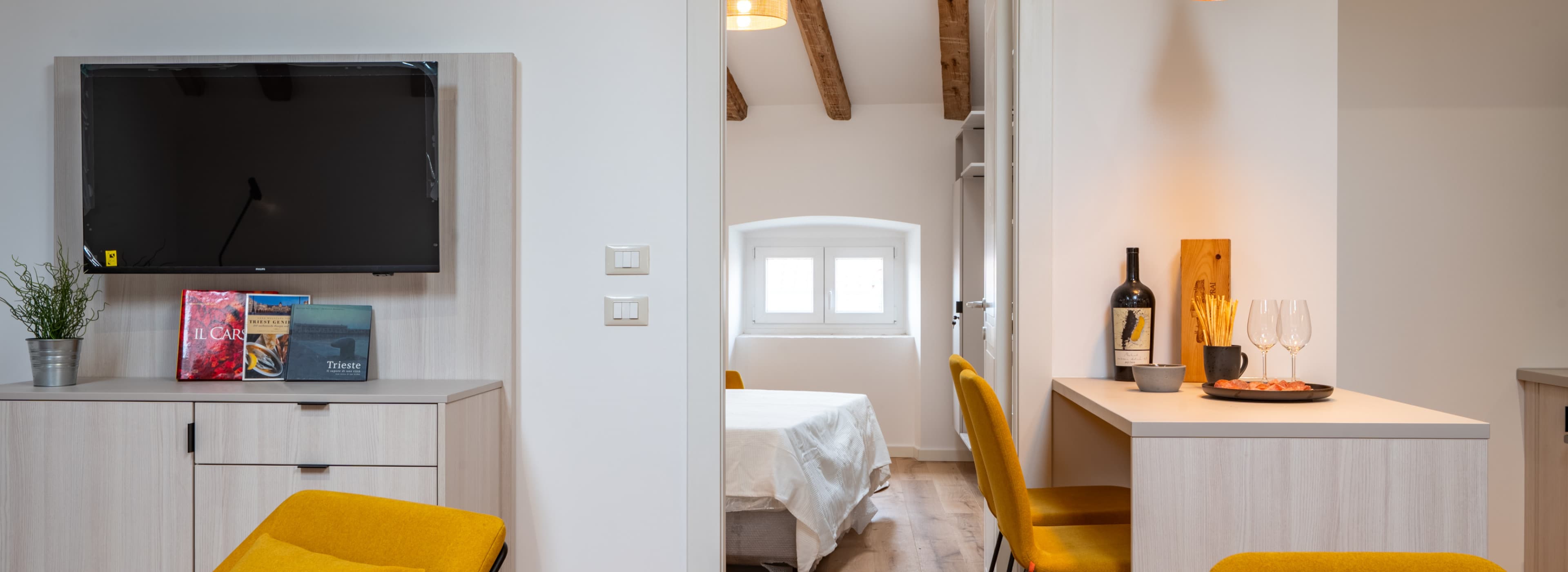 Blick in das abgetrennte Schlafzimmer, während die Farbe eines warmen Gelbes verschiedene Akzente in der gesamten Wohnung setzt.