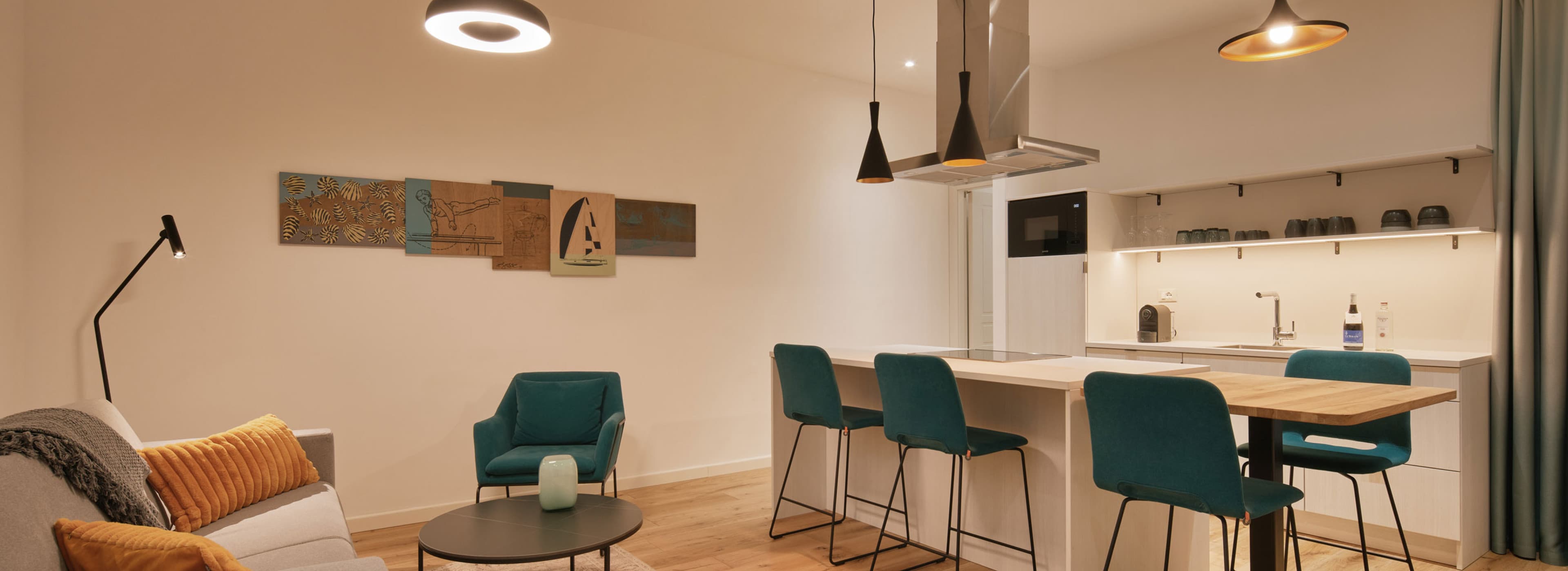 Si vedono la cucina e la zona giorno dello Spacy Studio. Sul lato sinistro c'è un divano che può essere trasformato in letto e di fronte, all'isola della cucina, gli ospiti possono sedersi e godersi la colazione, il pranzo o la cena.