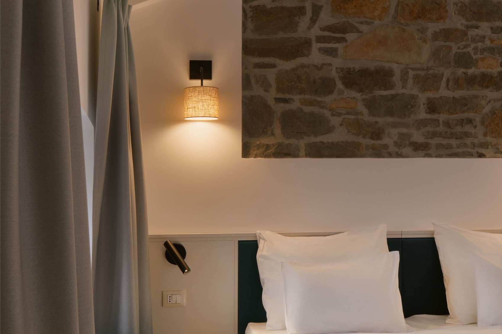 Nella foto è raffigurata la camera da letto splendidamente restaurata di un monolocale confortevole, che presenta una parete in mattoni a vista nella parte posteriore del letto. Anche le travi in legno del soffitto conferiscono alla stanza un certo calore.