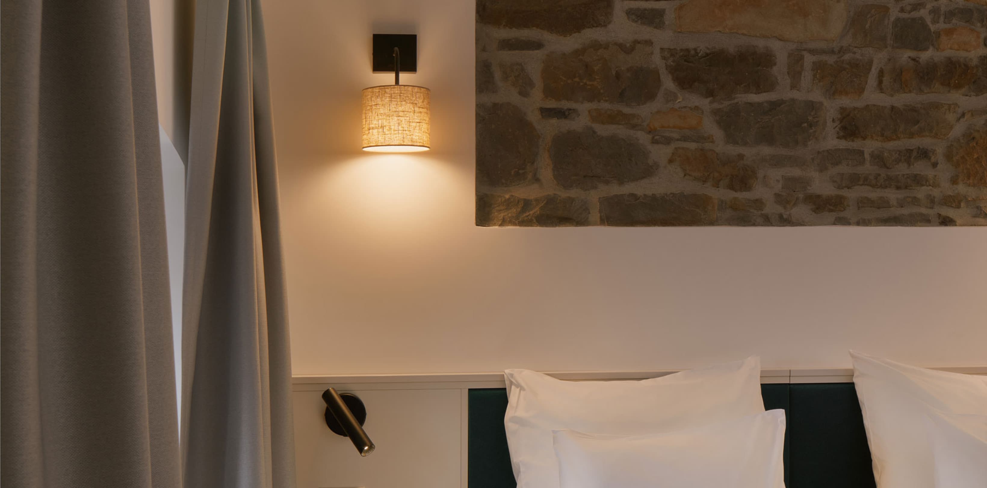 Das Foto zeigt das wunderschön renovierte Schlafzimmer eines gemütlichen Studios mit einer offenen Backsteinwand hinter dem Bett. Die Holzbalken an der Decke verleihen dem Raum zusätzlich eine gewisse Gemütlichkeit.