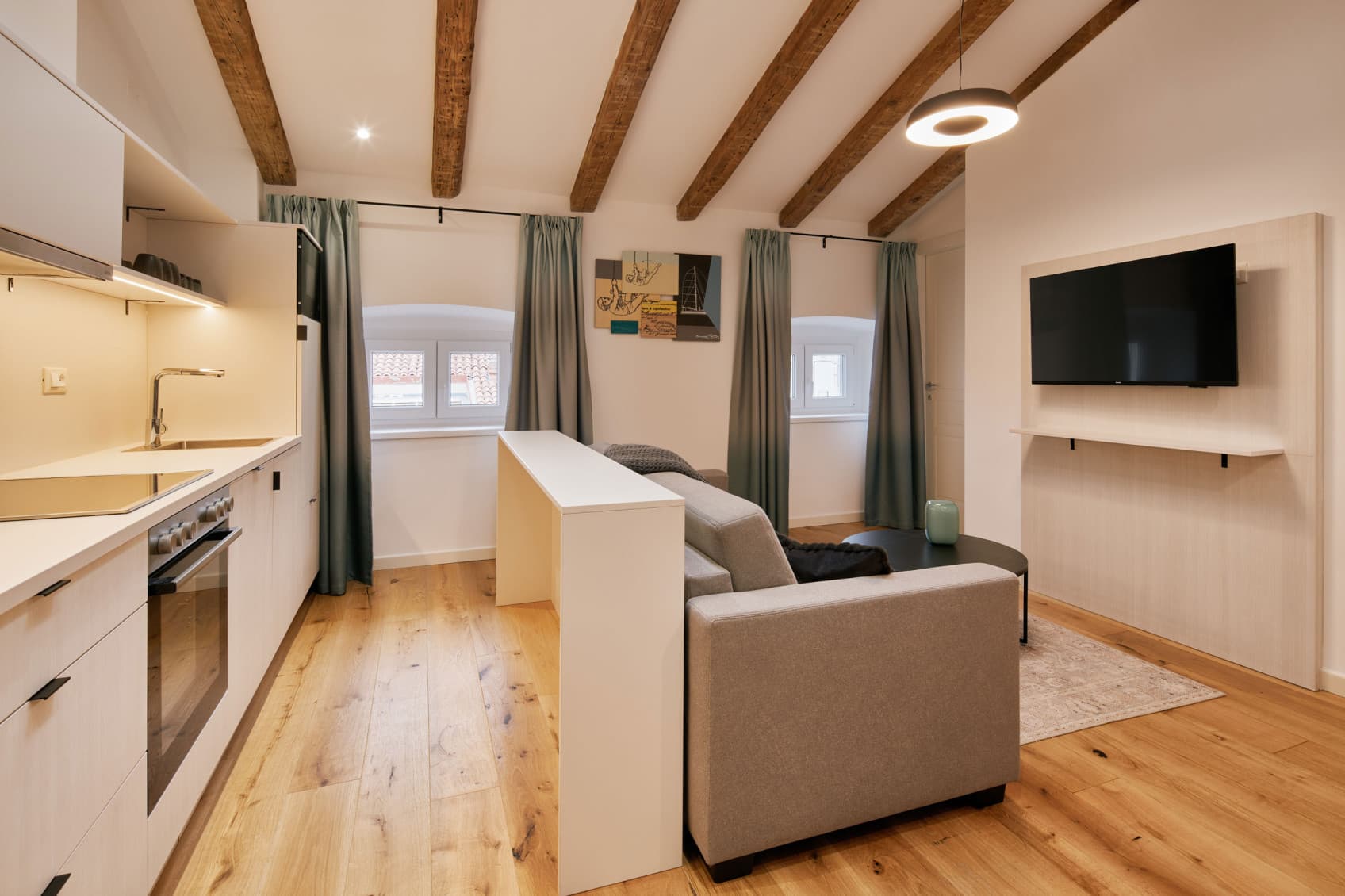 Nella foto è raffigurato il soggiorno del Comfy Studio, con sul lato destro un divano per rilassarsi e la TV. Sul lato sinistro, possiamo vedere una cucina completamente attrezzata che offre ampio spazio per preparare un pasto completo, come la colazione o la cena.