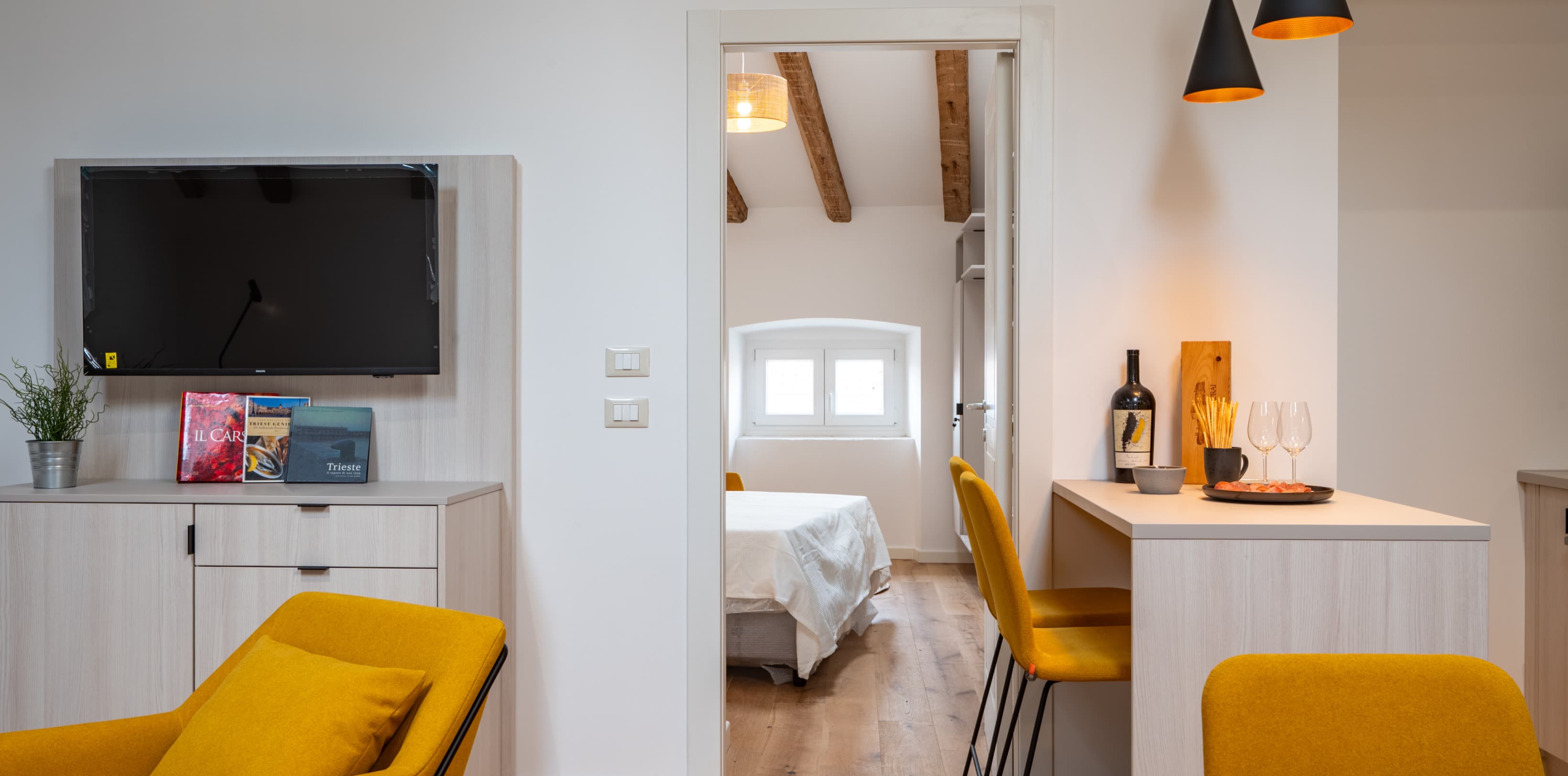 Blick in das abgetrennte Schlafzimmer, während die Farbe eines warmen Gelbes verschiedene Akzente in der gesamten Wohnung setzt.