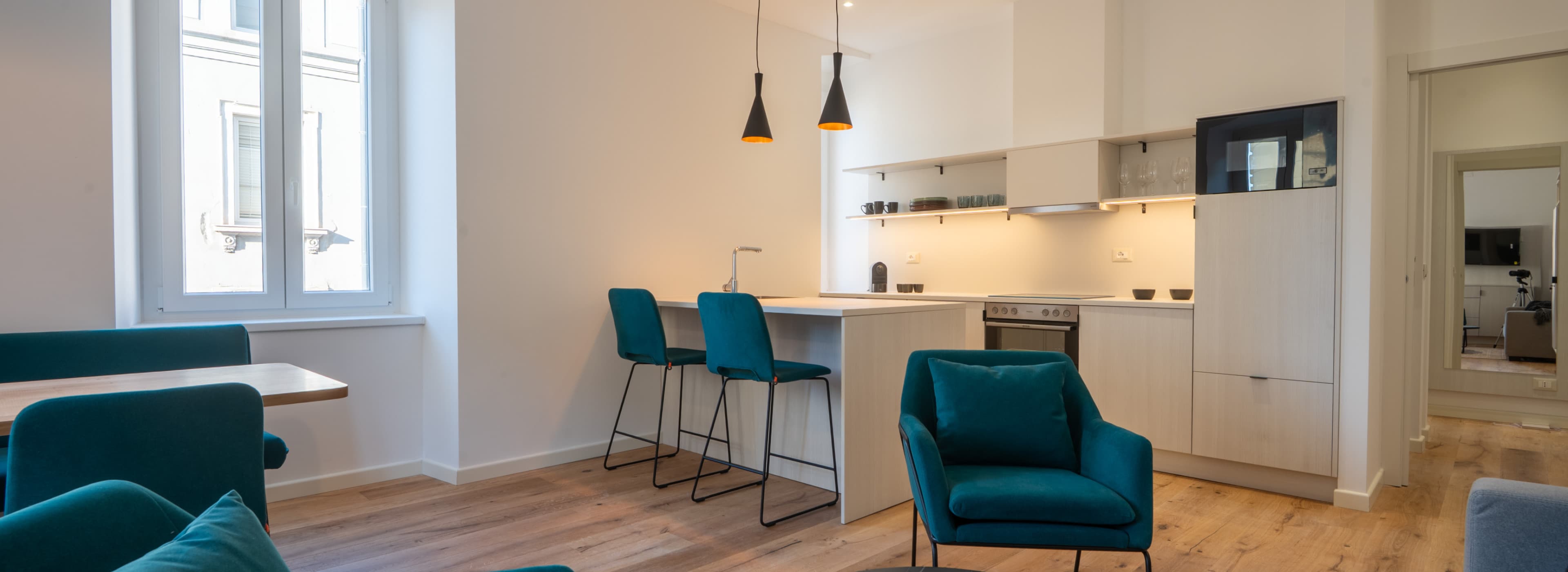 Die Abbildung zeigt einen Blick in den offenen Küchen- und Wohnbereich, in dem die Sessel und die Inneneinrichtung die Farbe Dunkelgrün haben.