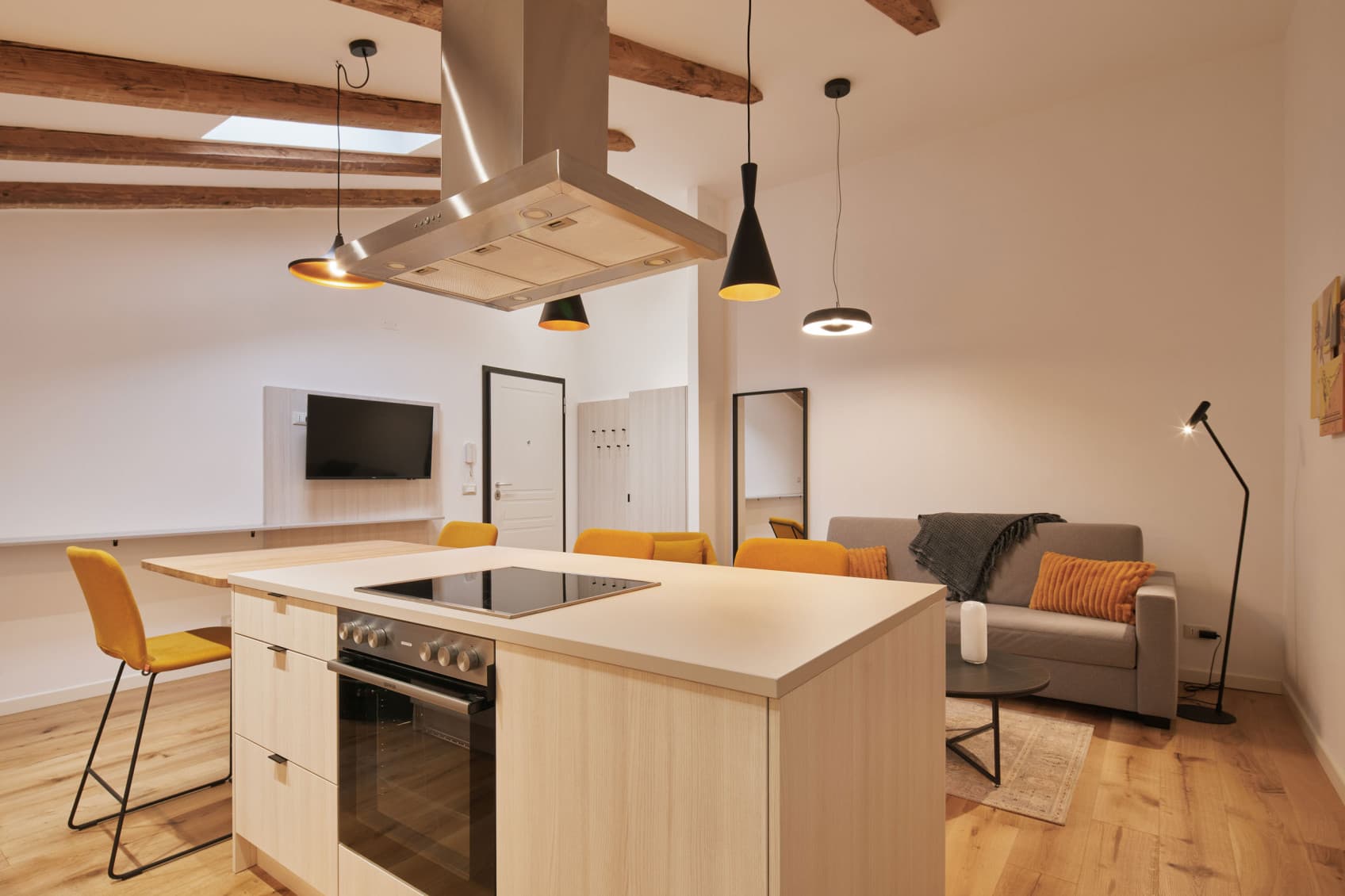 Nella foto è raffigurata la cucina dello studio Spacy, con un'isola di cottura nella parte anteriore e centrale della stanza. Sullo sfondo è possibile vedere il divano, che può essere trasformato anche in letto.