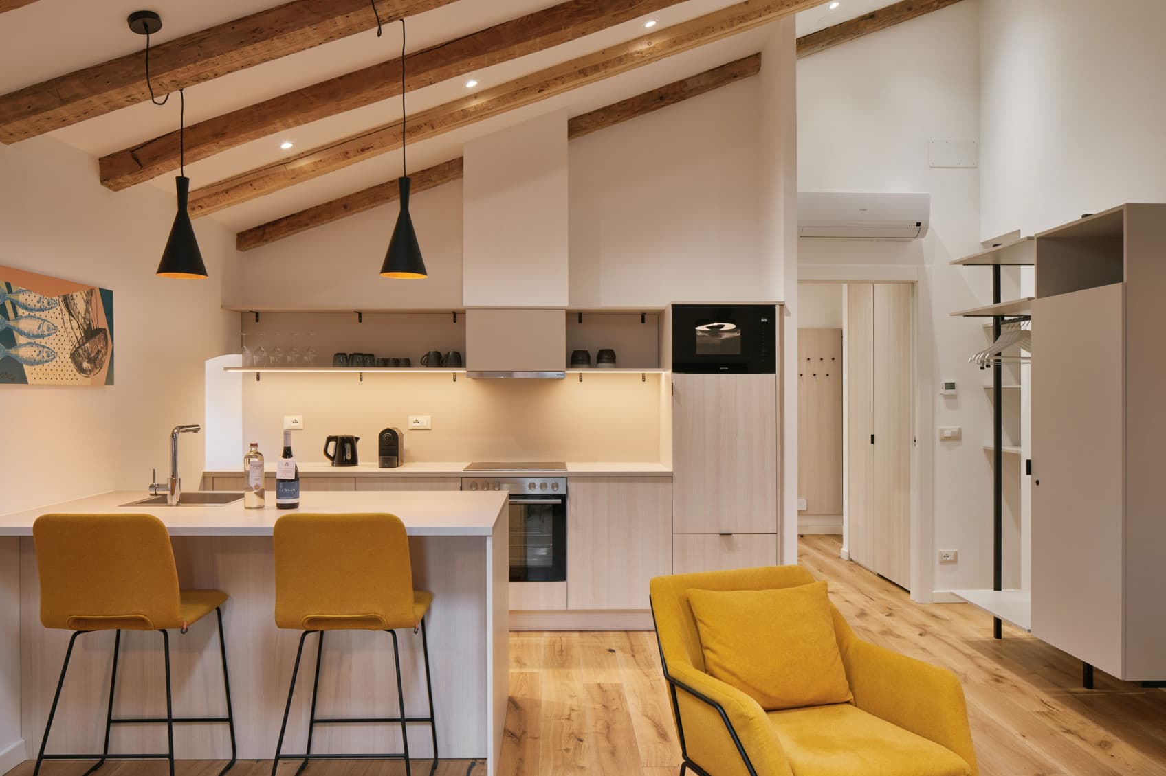 Si vede lo spazioso monolocale all'ultimo piano con il bellissimo soffitto in legno ristrutturato. La cucina completamente attrezzata è incassata nell'angolo sotto il soffitto.