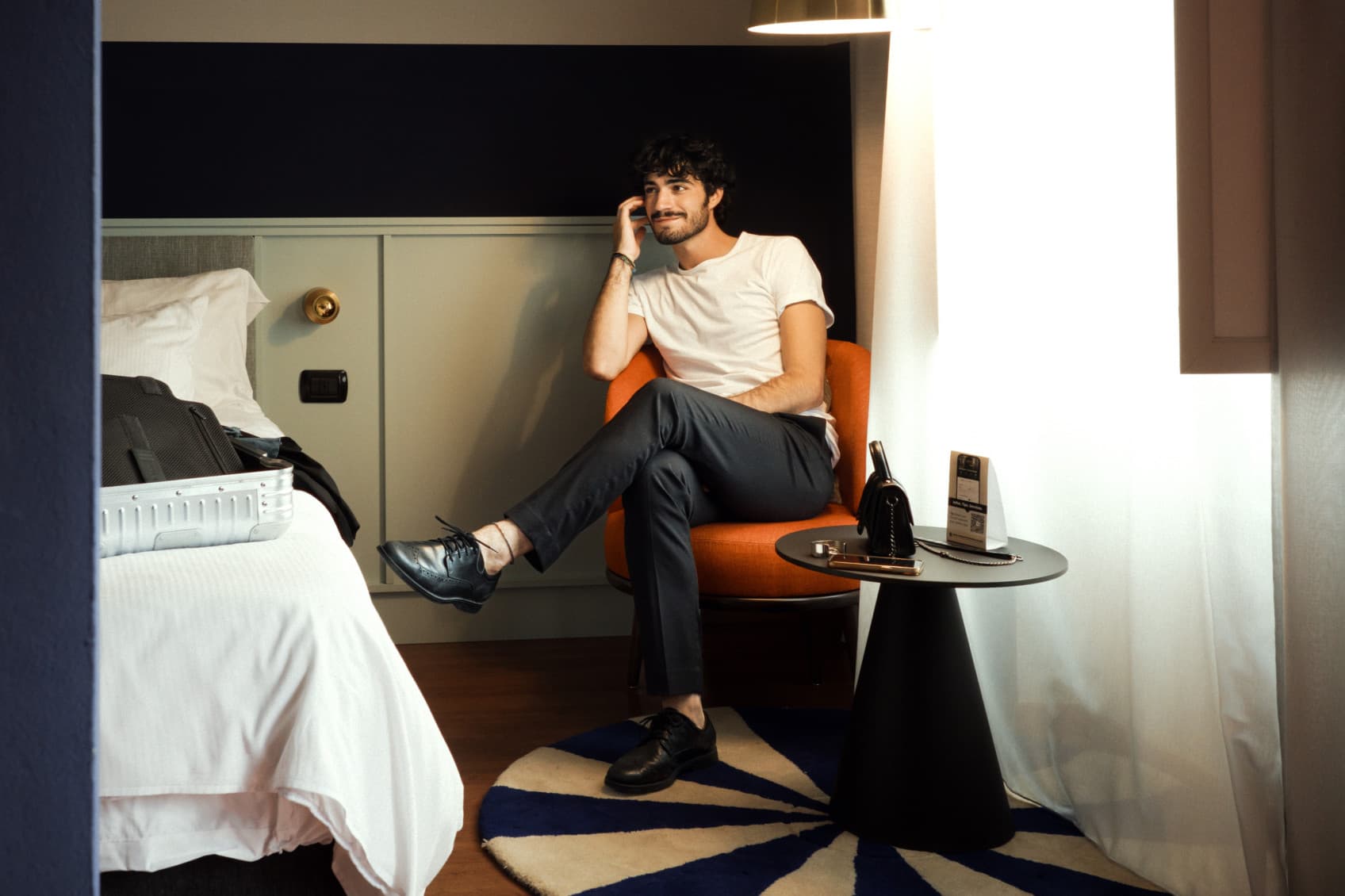 A man is sitting on an armchair in one of the studios of URBANAUTS smiling towards a second person, while relaxing after arrival.