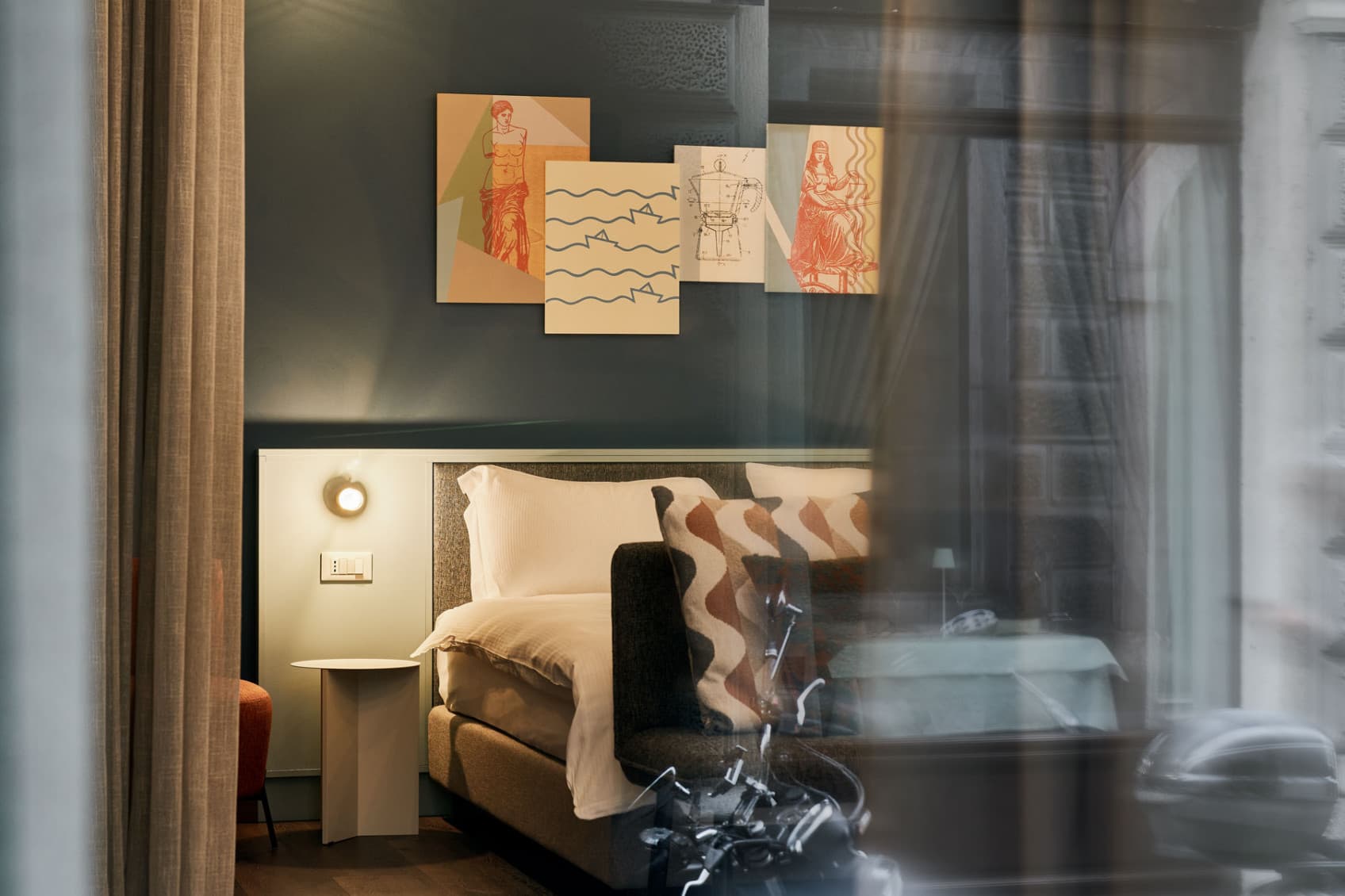 Blick durch das große Fenster auf die Street Lofts zur Straße hin. Im Hintergrund sind das Bett und Kunstwerke zu sehen, die die Individualität der verschiedenen Street Lofts widerspiegeln.