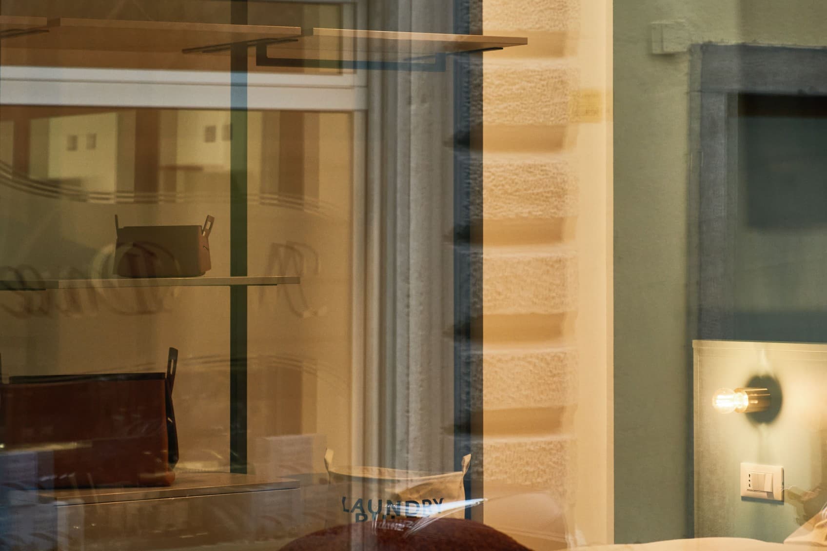 Blick durch das Außenfenster ins Schlafzimmer. Man sieht das Bett sowie den offenen Raum im Hintergrund mit einem offenen Kleiderschrank.