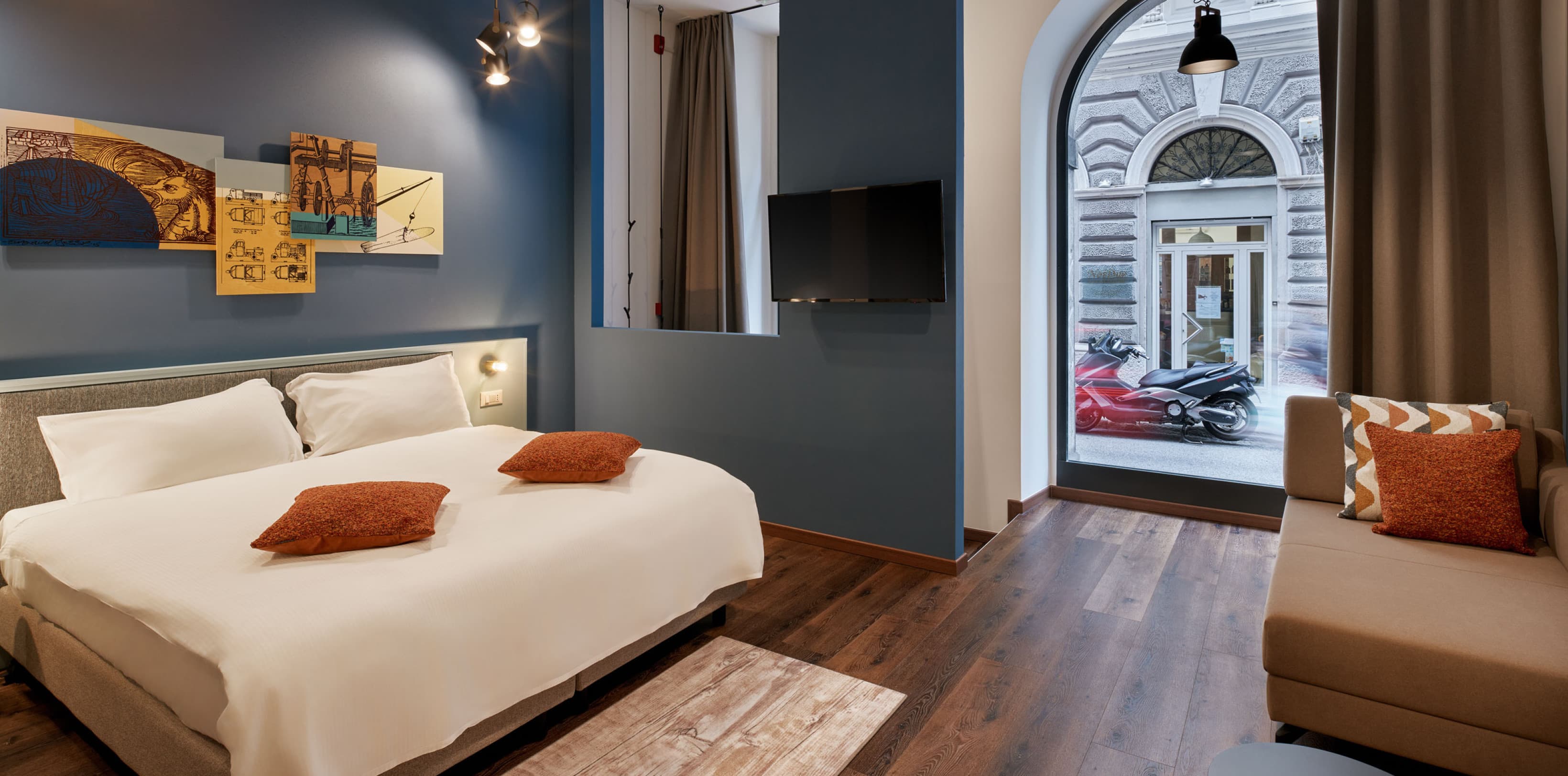 Nella foto sono visibili la camera da letto e la zona giorno, che costituiscono un unico grande soppalco al piano terra. Sul lato sinistro si trova un grande letto matrimoniale, mentre il divano è situato sul lato destro del soppalco. Guardando dritto davanti a sé, si può vedere la grande vetrina che dà sulla strada.