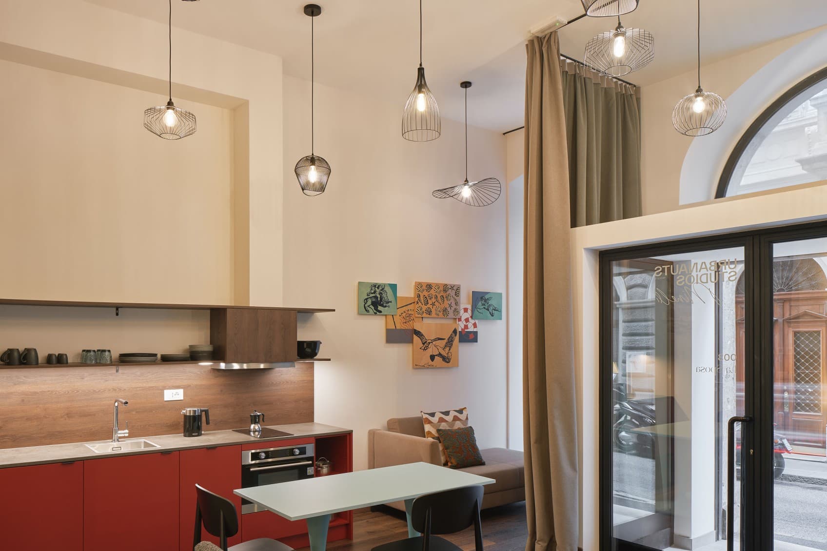 Seen is the open space living area of one of the lofts. The view is towards the open entrance, which is facing the street on the ground floor. In the background is a kitchenette and table to have dinner, while the high ceilings open up the space even more.